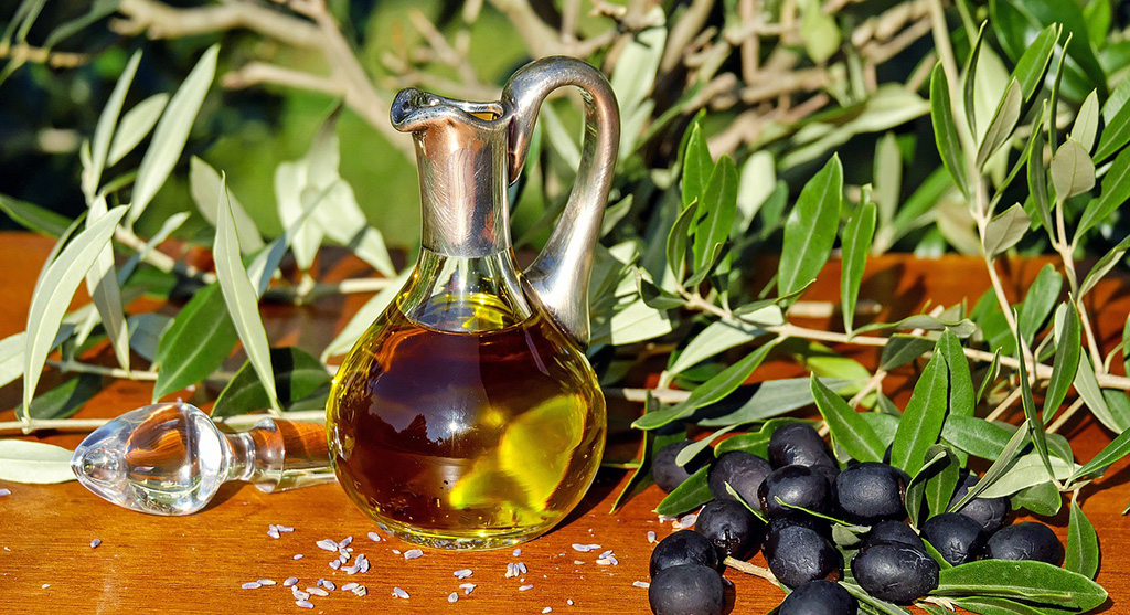 Olive and oil in a glass jug next to a tree